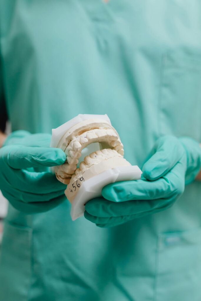 Uşak Zirkonyum Kaplama ve Estetik Gülüş Tasarımı Close-up of dentist in scrubs holding a dental cast in a clinic setting.
